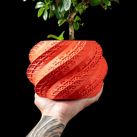 Red twisted leaf 3D printed PLA planter with geometric spiral texture, held by hand, featuring small bonsai plant, artistic design by Plantale.