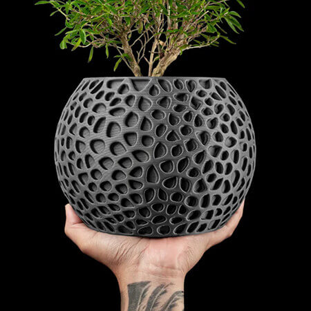 Modern black textured 3D printed PLA planter with geometric hollow pattern, held by hand, showcasing green bonsai plant, by Plantale.