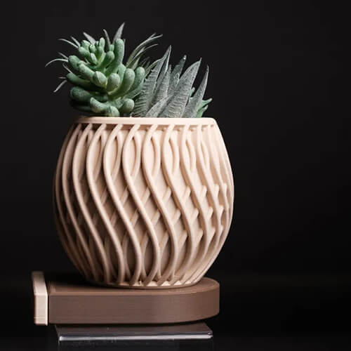 Beige 3D-printed planter with an intricate twisted wave pattern, holding a mix of small succulents, displayed on a brown stand against a dark background.