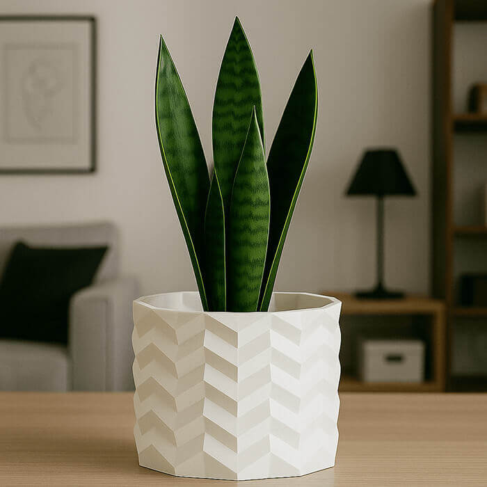 Modern white geometric 3D printed PLA planter with snake plant on a wooden table in a living room setting.