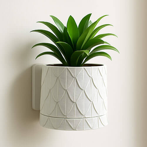 A white wall-mounted planter with a subtle leaf-pattern texture, holding a small green plant with layered, pointed leaves, displayed against a clean indoor wall.