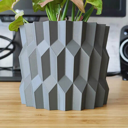 Gray diamond 3D printed PLA planter with geometric faceted design, holding green plant on wooden desk, modern minimal decor by Plantale.