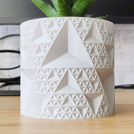 White endless triangle 3D printed PLA planter with geometric pyramid pattern, holding green indoor plant, modern faceted design by Plantale.