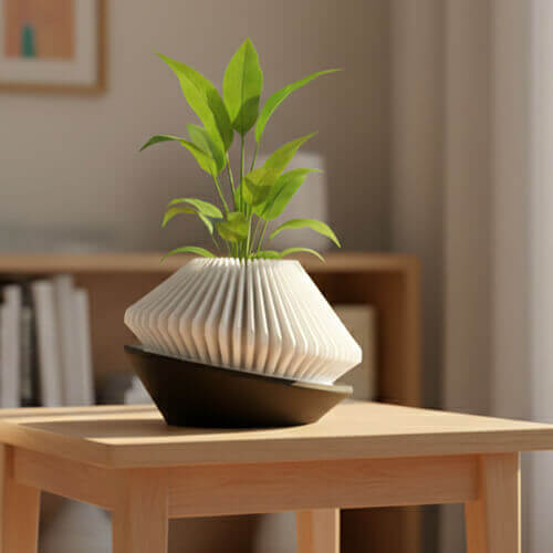 Modern geometric white tabletop planter with ribbed texture placed at an angle on a black base, holding a small green plant on a wooden table in a softly lit room.