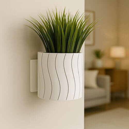 White wall-mounted planter with subtle wavy line texture, holding tall green ornamental grass, displayed in a softly lit modern living room.